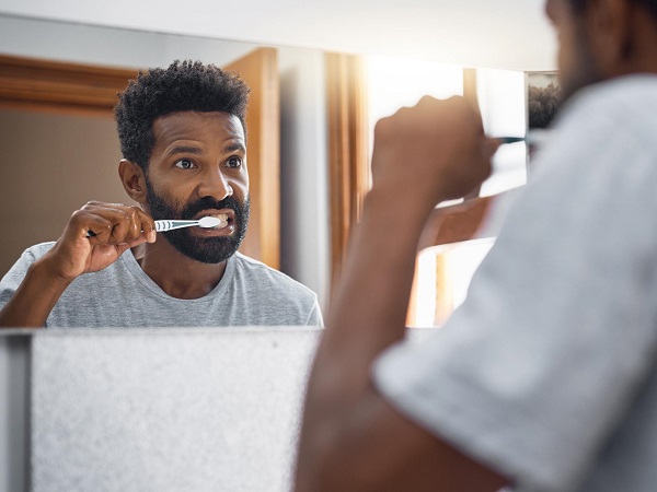 A man brushing his teeth and looking at mirror in the bathroom before he goes for a cycle ride.
